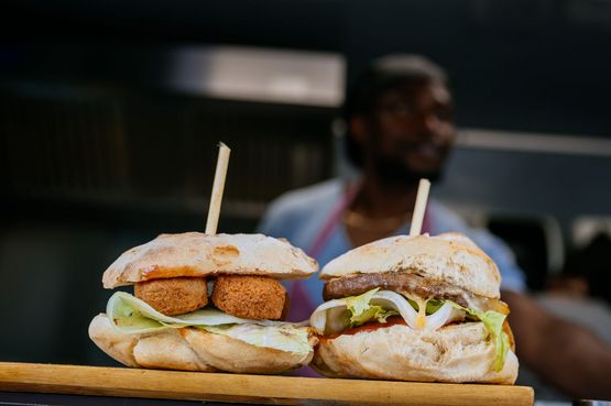 Zwei Burger auf einem Holzbrett. Ein Burger ist mit Falaffel und Salat belegt, der andere mit einem Stück Fleischu und Salat.