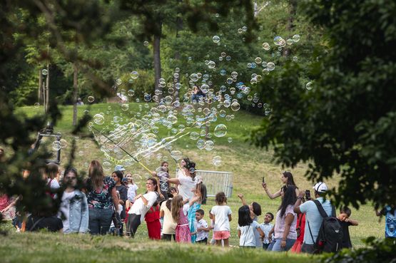 Kinder springen über eine Wiese während über ihnen unzählige Seifenblasen durch die Luft schweben