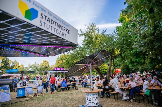 Ein Solar-Sonnenschirm mit Beleuchtung steht auf einer Sommerwiese. Auf dem Sonnenschirm ist das Logo der Stadtwerke Stuttgart.