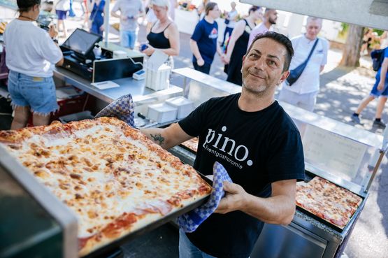Ein Mitarbeiter eines Food-Standes schiebt gerade ein großes Blech Pizza in den Ofen.
