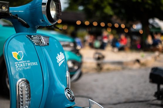 Im Vordergrund steht ein blauer Stella E-Roller der Stadtwerke, kunstvoll in Szene gesetzt
