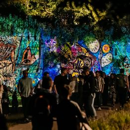 Menschen laufen an Lichtprojektionen an einer Wand vorbei.